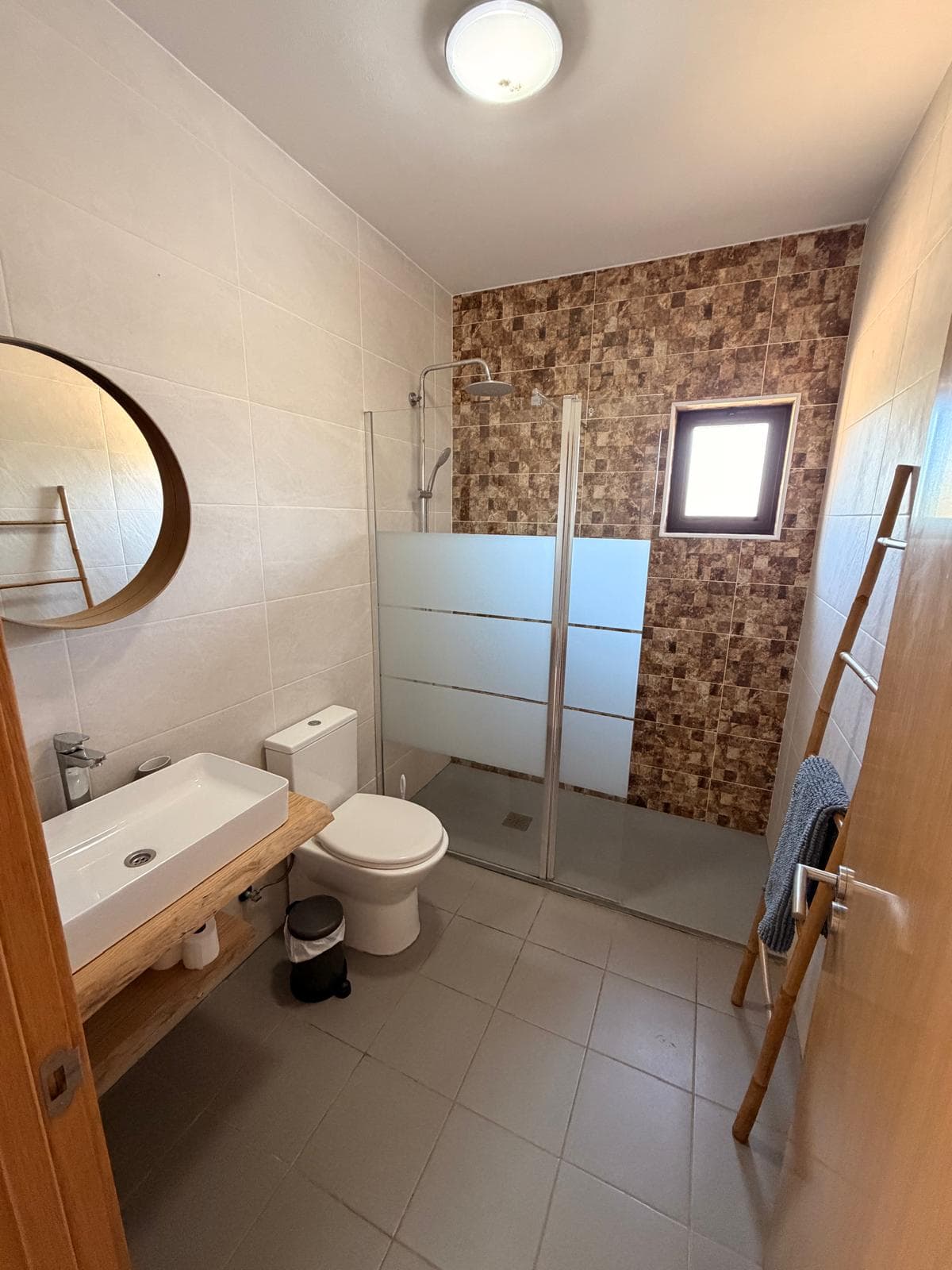 Casa de banho com base de duche, espelho redondo e bancada de madeira