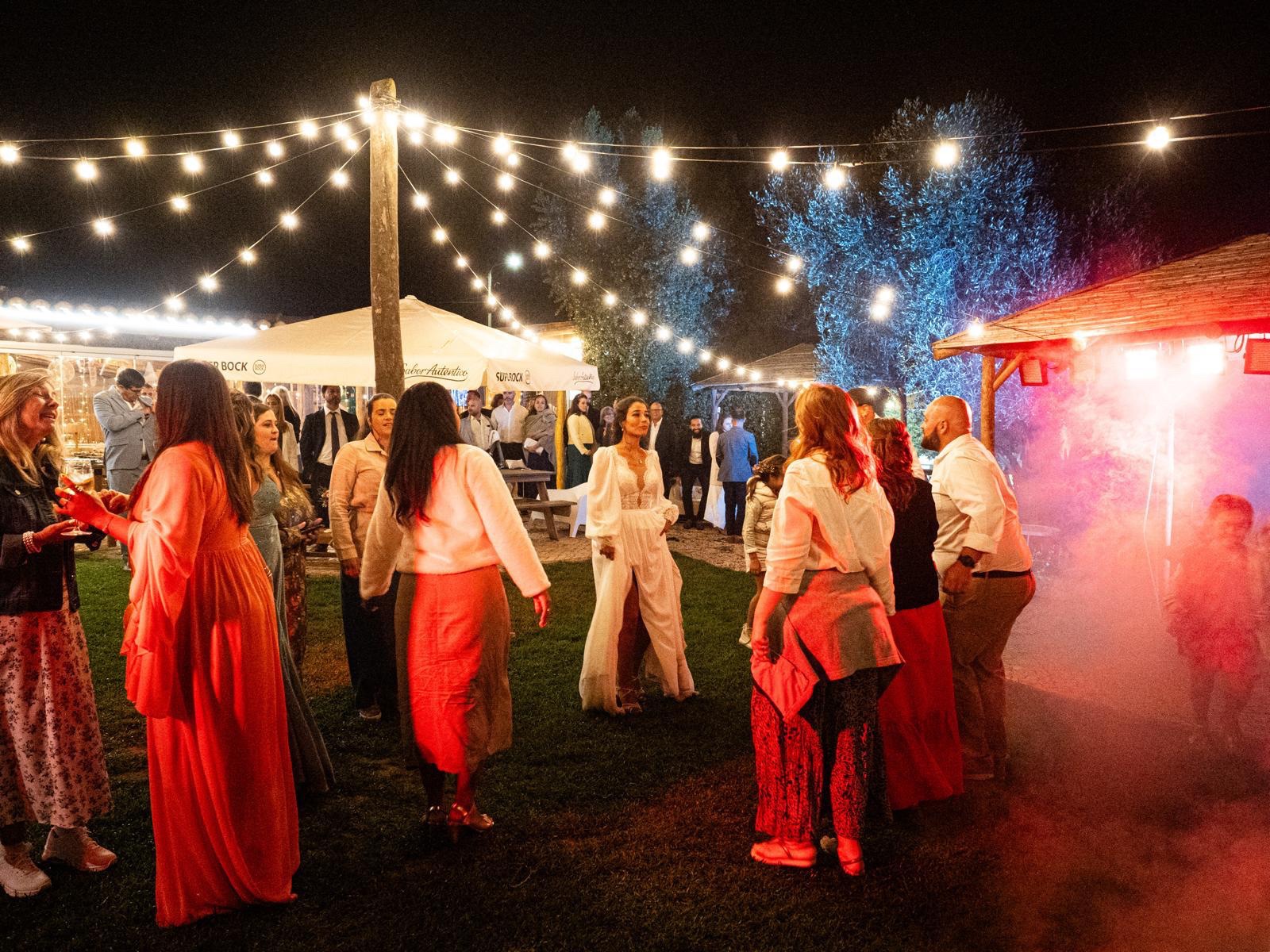 O jardim à noite, com luzes penduradas sobre a pista tomada de convidados e fumo colorido