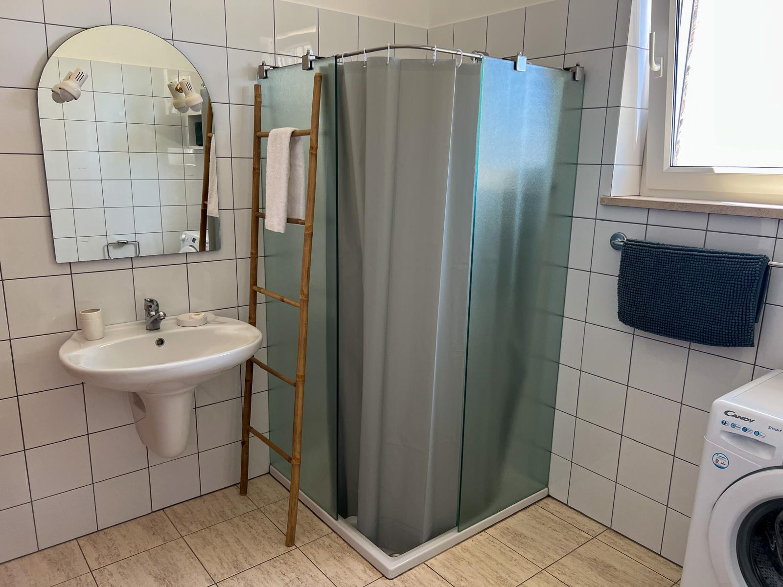 Casa de banho com duche de vidro fosco e máquina de lavar roupa