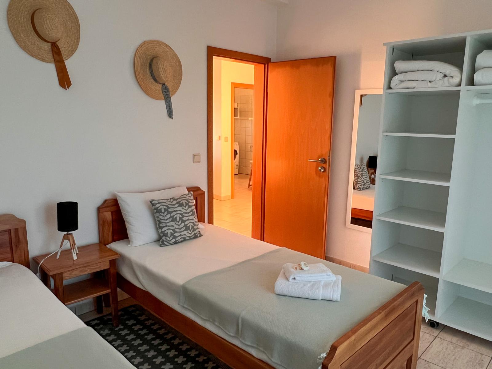 Quarto de duas camas individuais, com chapéus de palha na parede